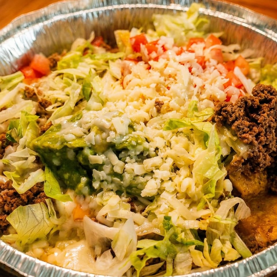 Loaded taco salad in a foil bowl with seasoned beef, lettuce, tomatoes, avocado, melted cheese, and tortilla chips.